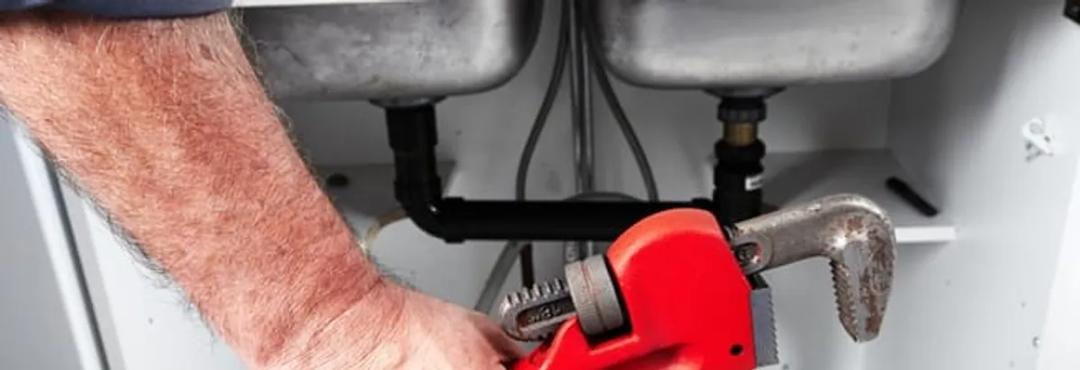 Garbage disposal repair technician tightening drain connections under a kitchen sink in Arlington, TX